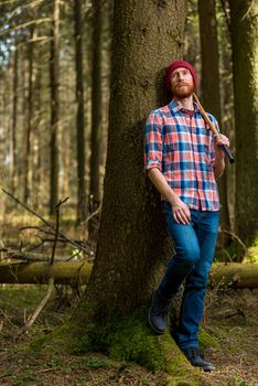 tired lumberjack with an ax resting, leaning against a tree