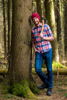 a smiling forester with an ax resting, leaning against a tree