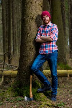 a man with a beard - a forester resting with an ax, leaning against a tree