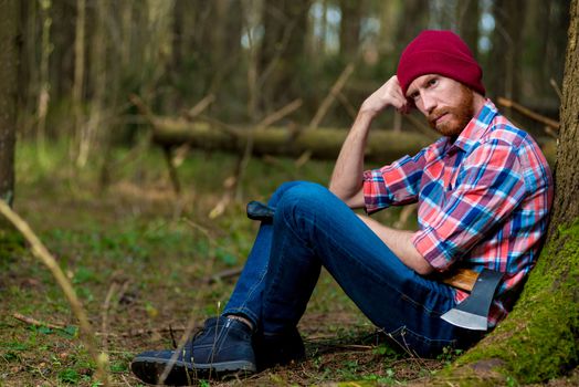 pensive bearded lumberjack on vacation near a tree in the forest