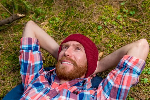 happy dreaming forester with a red beard on a forest glade resting