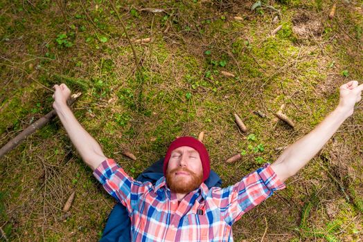 thoughtful hipster stroking his red beard, a portrait of a curtain, a man lying on the ground in the forest
