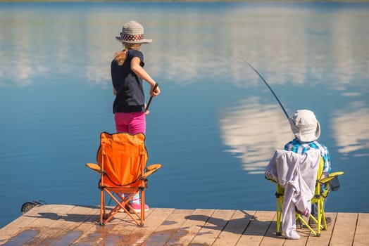 brother and sister are fishing on a wooden pier without adults