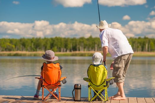 Father with his son and daughter on a wooden pier in the lake fishing with fishing rods