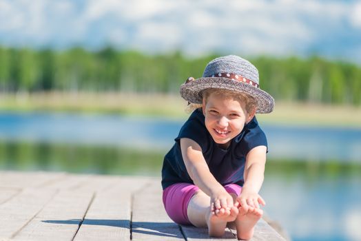 happy girl in a hat sits on a wooden pier near the lake and poses