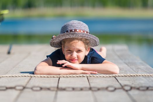 portrait of a girl in a hat on a wooden pier near the lake