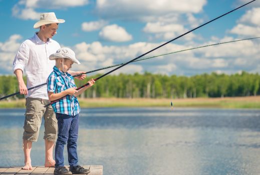 father and son with fishing rods on a wooden pier near the lake on a sunny day