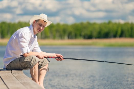 experienced fisherman sitting on a wooden pier and fishing in the lake
