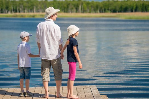 Dad with his son and daughter admiring the beautiful scenic lake, the view from the back