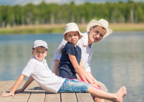 happy family is resting on a wooden pier near the lake