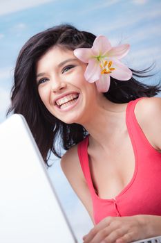 Beautiful laughing girl with lilium in her hair behind laptop