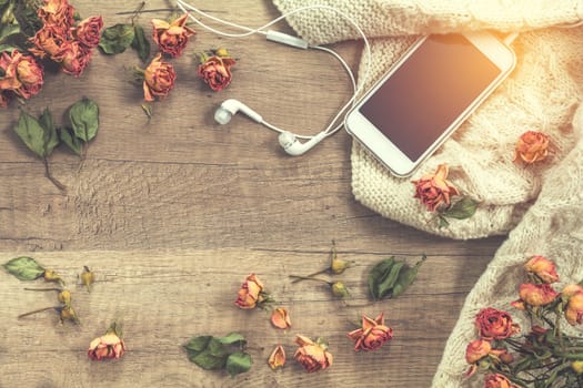 White knitting wool, dried roses flowers, mobile phone and headphones. Beautiful romantic female’s background. Toned in instagram style.