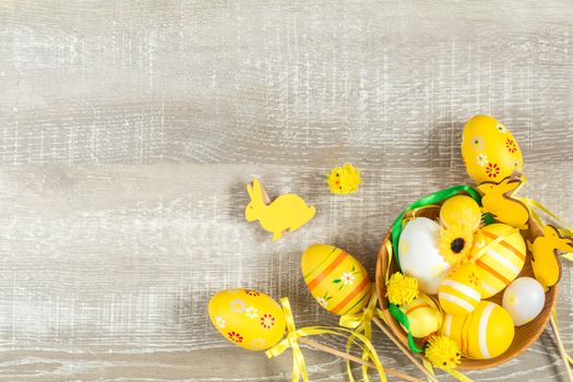 Composition with painted eggs and other easter attributes and accessories in yellow tones on a light wooden surface. Top view, copy space.