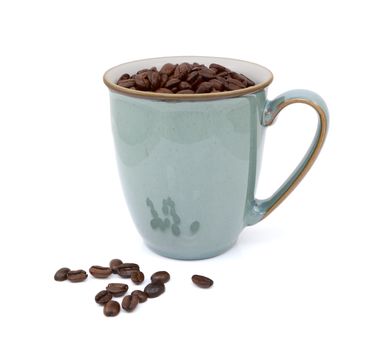 Dark roasted coffee beans in green mug and spilled beside, on a white background