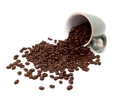 Aromatic roasted coffee beans pouring out from a green china mug on a white background