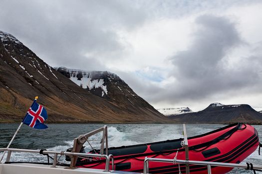 Icelandic flag and rubber boat sailing in a fjord with mountains background, Iceland