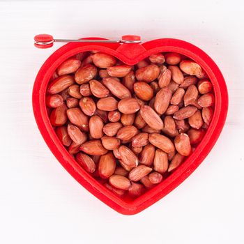 Raw peanuts in heart bowl on the white background