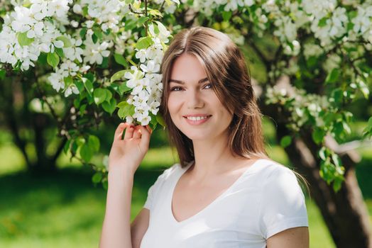 Beautiful young brunette woman standing near blooming apple tree