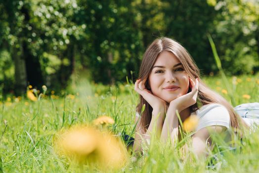 Beautiful young woman laying on grass with dandelion flowers in park