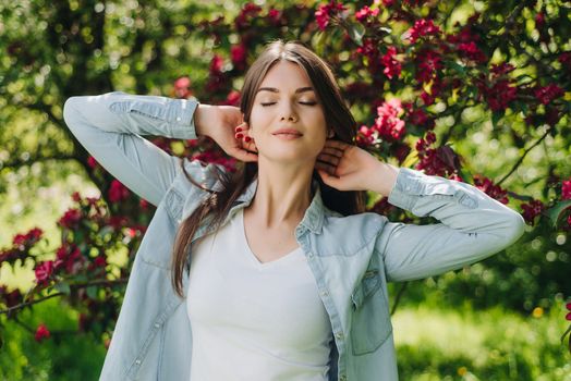 Beautiful young brunette woman standing near blooming tree with red flowers