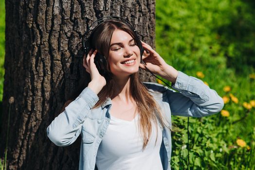 Young brunette woman with headphones listening to the music in park on sunny summer day