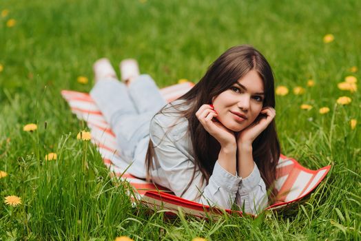 Beautiful young woman laying on grass with dandelion flowers in park