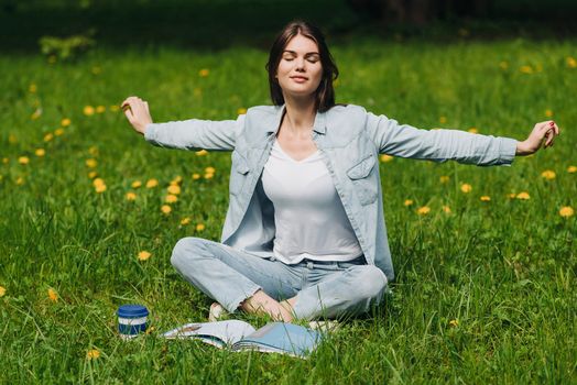 Beautiful young woman enjoy nature sitting in park with book and coffee