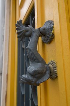decorative fish door handle on a yellow wooden door.