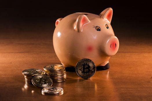 Piggy bank with bitcoins on top of wooden table.