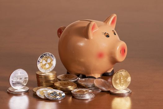 Piggy bank with several crypto currency coins on top of wooden table.