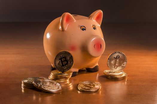Piggy bank with bitcoins on top of wooden table.