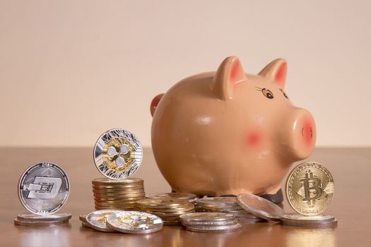 Piggy bank with several crypto currency coins on top of wooden table.