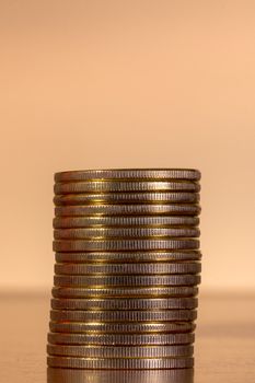 Vertical pile of golden coins on top of wooden table.