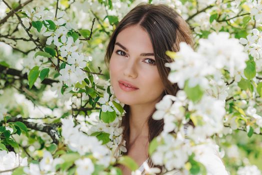 Beautiful young brunette woman standing near blooming apple tree