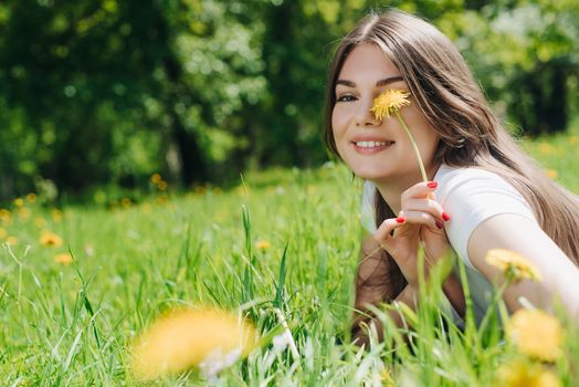 Beautiful young woman laying on grass with dandelion flowers in park