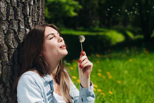 Beautiful young woman with white dandelion in park