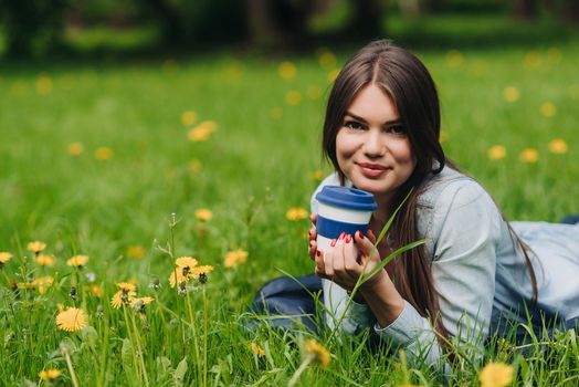 Beautiful young woman laying on the grass with cup of takeaway drink