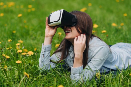 Woman using the virtual reality headset outdoors laying in spring flower field