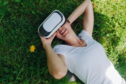 Woman using the virtual reality headset outdoors laying in spring flower field