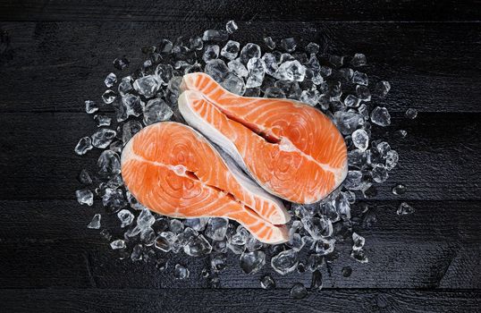 Salmon steak on ice on black wooden table top view. Fish food concept. Copy space