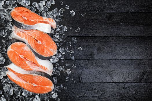 Salmon steaks on ice on black wooden table top view. Copy space