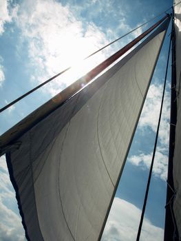 White sail against blue sky, clouds and sun ray