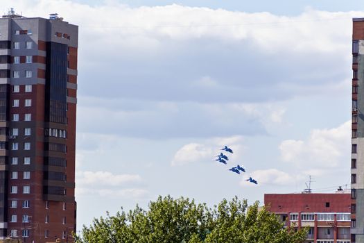 Six military airplanes are flying under city in blue sky