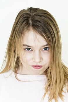 Cute angry girl with blond long hair on white wall in pink clothes