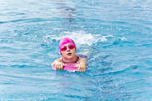 Cute girl with pink rubber hat are swimming in pool
