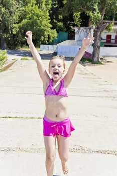 Running and screaming girl on the riverbank in pink swimsuit