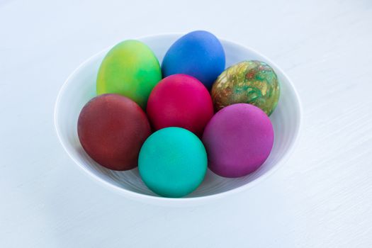 White plate of Easter multicolored boiled eggs decoration on wooden background