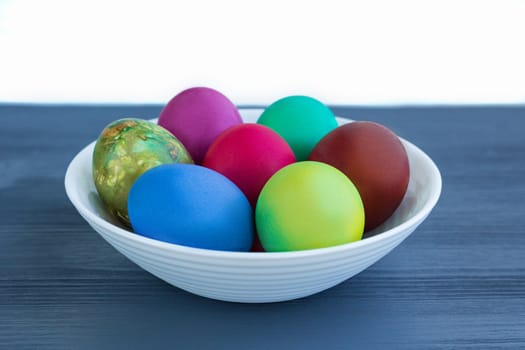 White plate of Easter multicolored boiled eggs decoration on grey wooden background