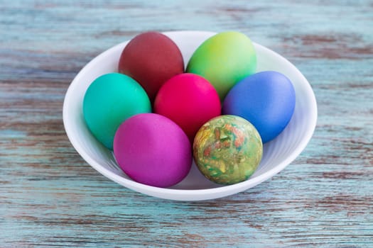 White plate of Easter multicolored boiled eggs decoration on wooden background
