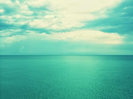 Retro image of sea and sky in green shades, with light coming through the clouds.